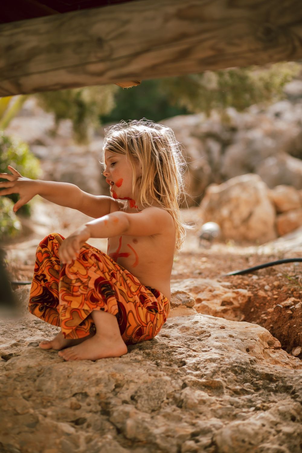 Child in orange ruffled dress playing on rocky terrain outdoors.