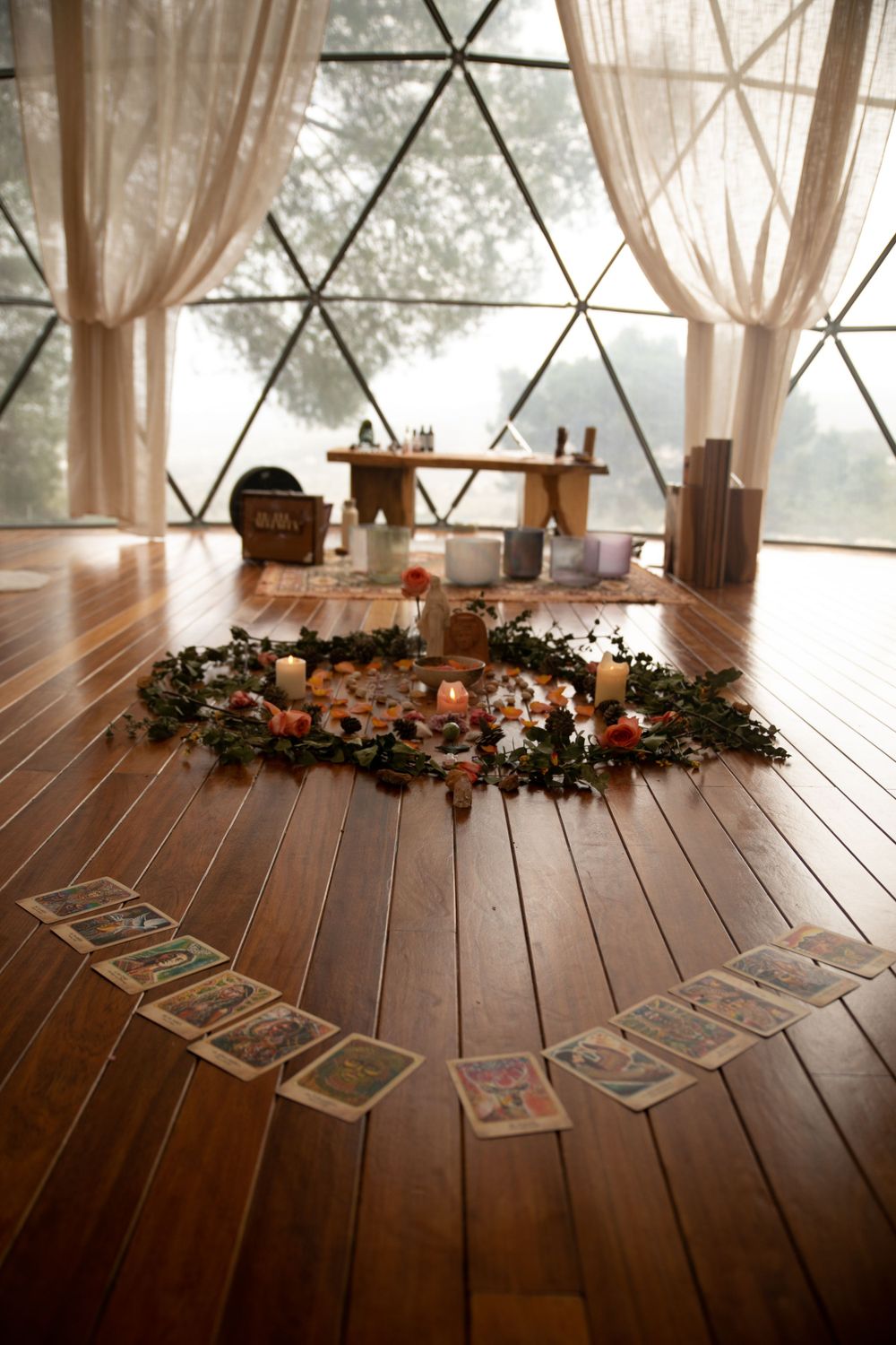 Tarot cards laid out in a curved line on a wooden floor with decorative floral arrangements.