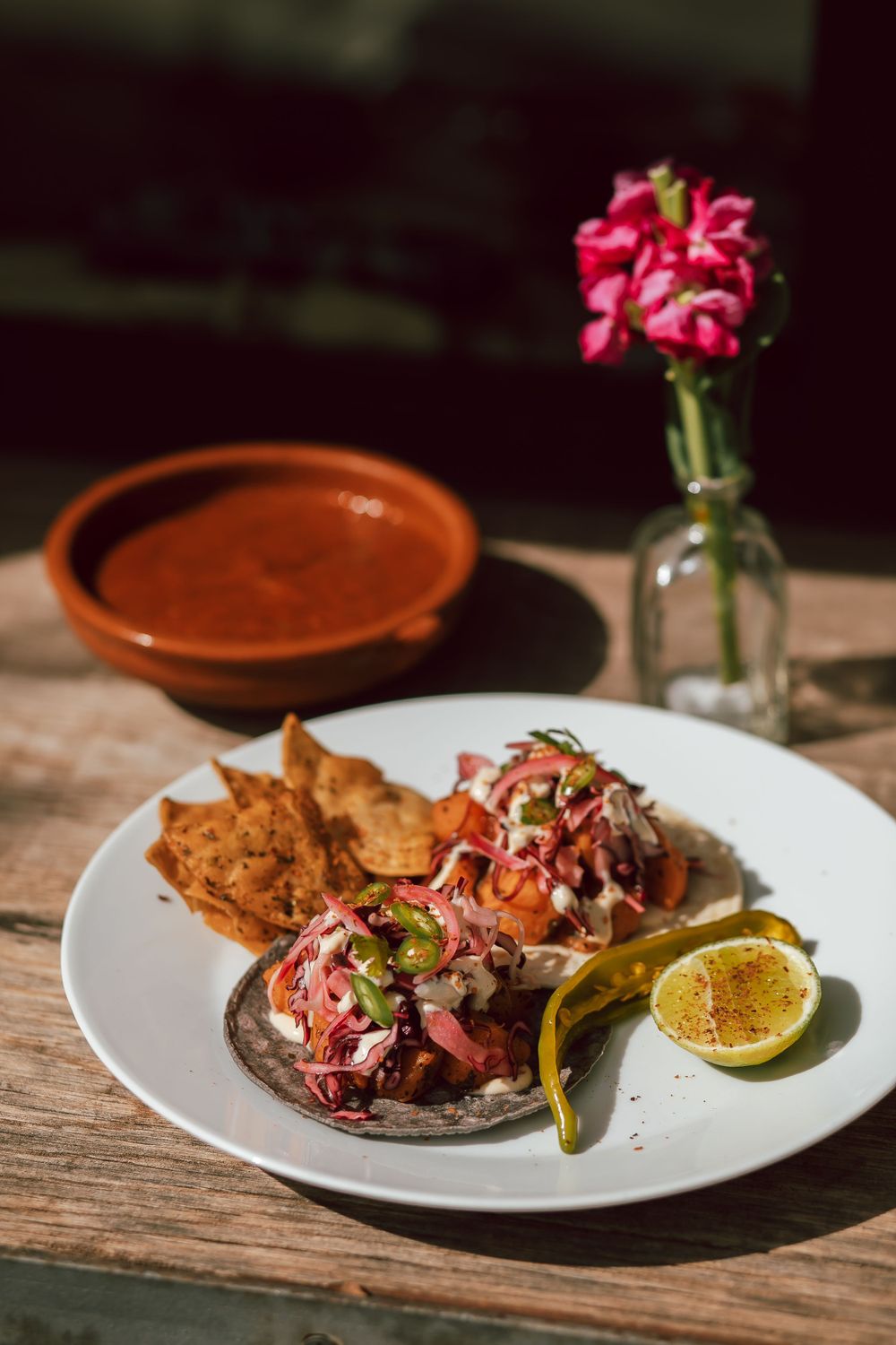 Artfully plated seafood dish with pink garnish and lime on rustic wooden table.