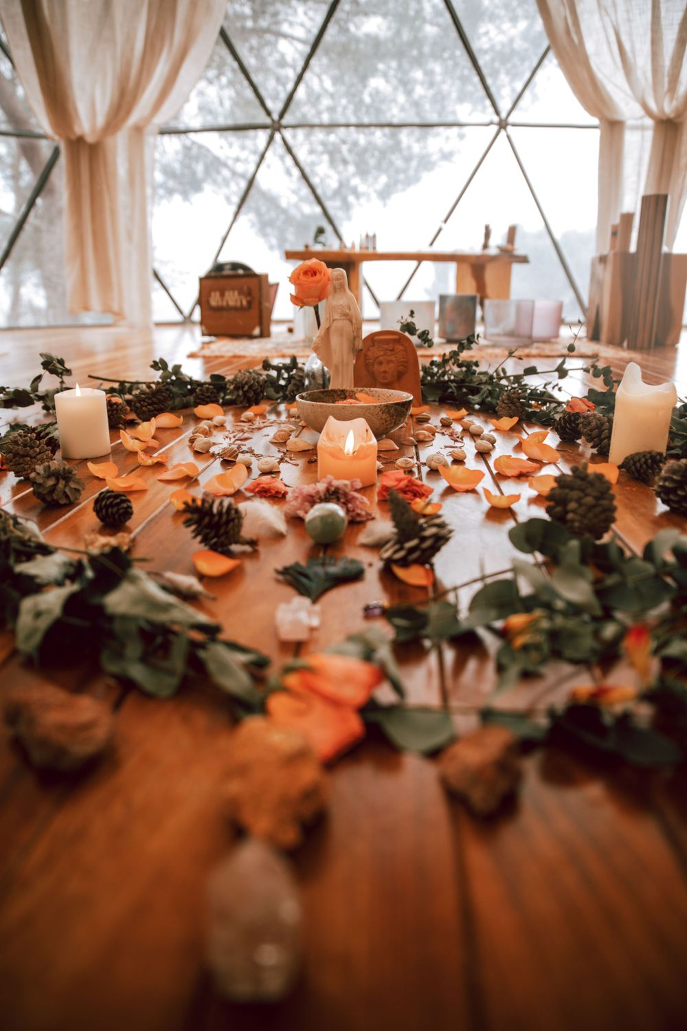 Decorative setup with candles and greenery on wooden flooring in a sunlit room.