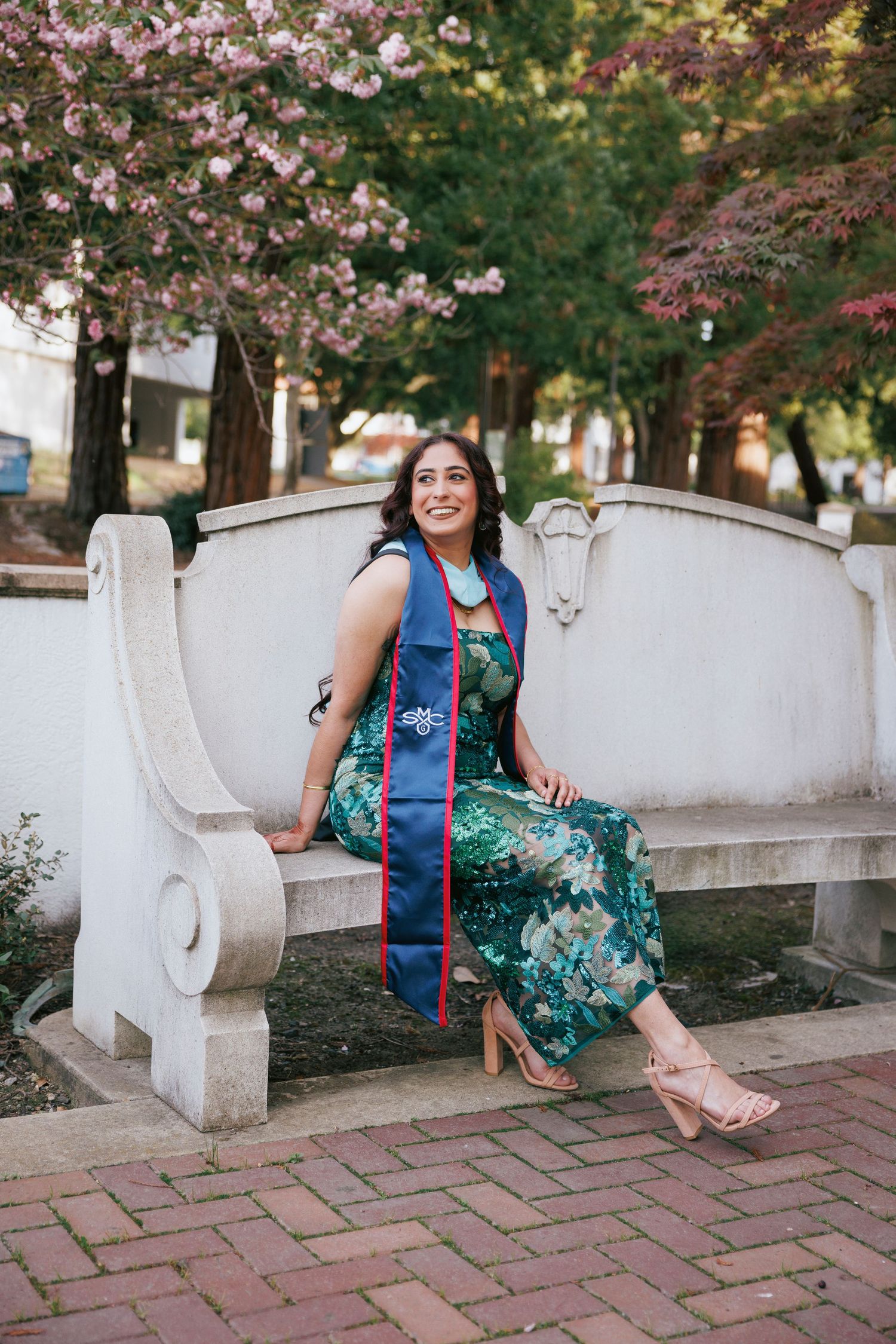 Graduate in blue gown jumps joyfully on beach while holding diploma.