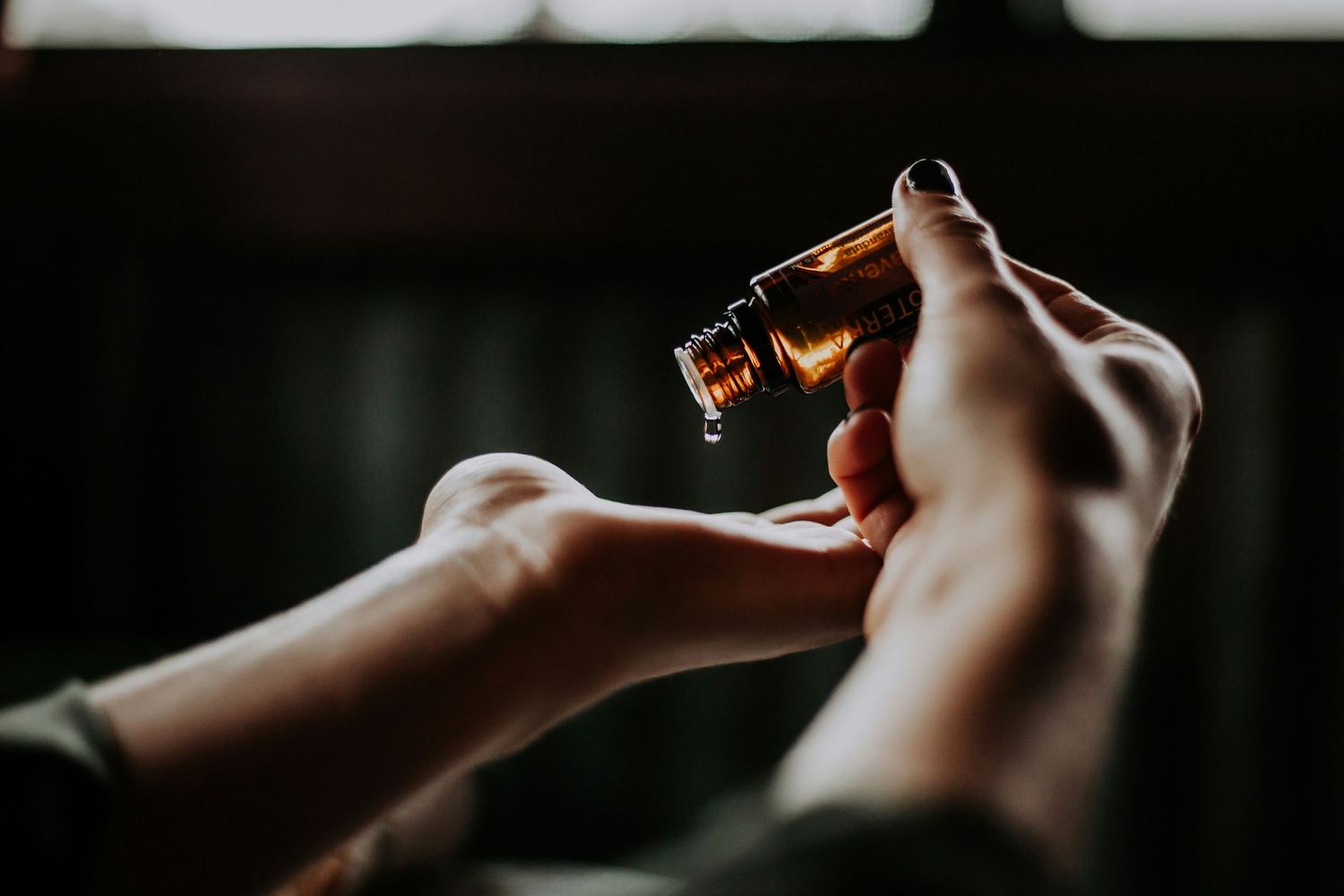 Hands holding an essential oil bottle in moody lighting against a dark background.