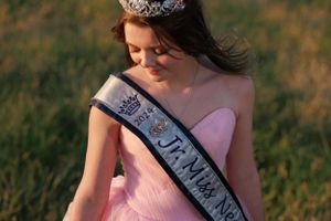 Jr. Miss Neoga is standing in her beautiful, pink ballgown, soaking up the light, in the horse pastures at Coyote Creek Tack and Stables.