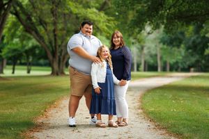 A family of 3 standing in a park during a beautiful summer day.