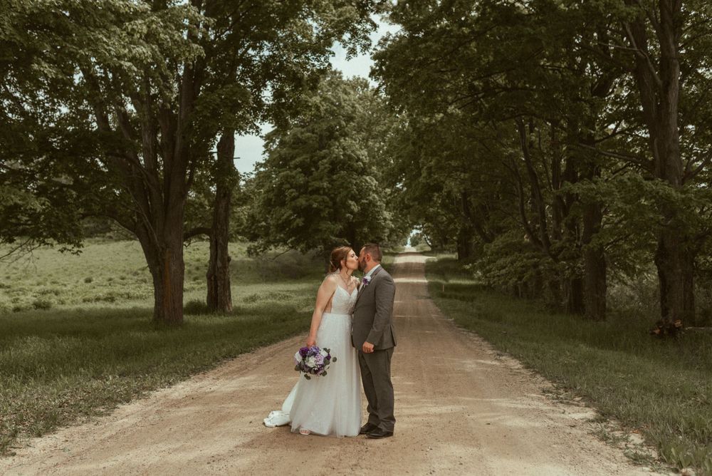 A couple shares their wedding day moment on a tree-lined dirt road.