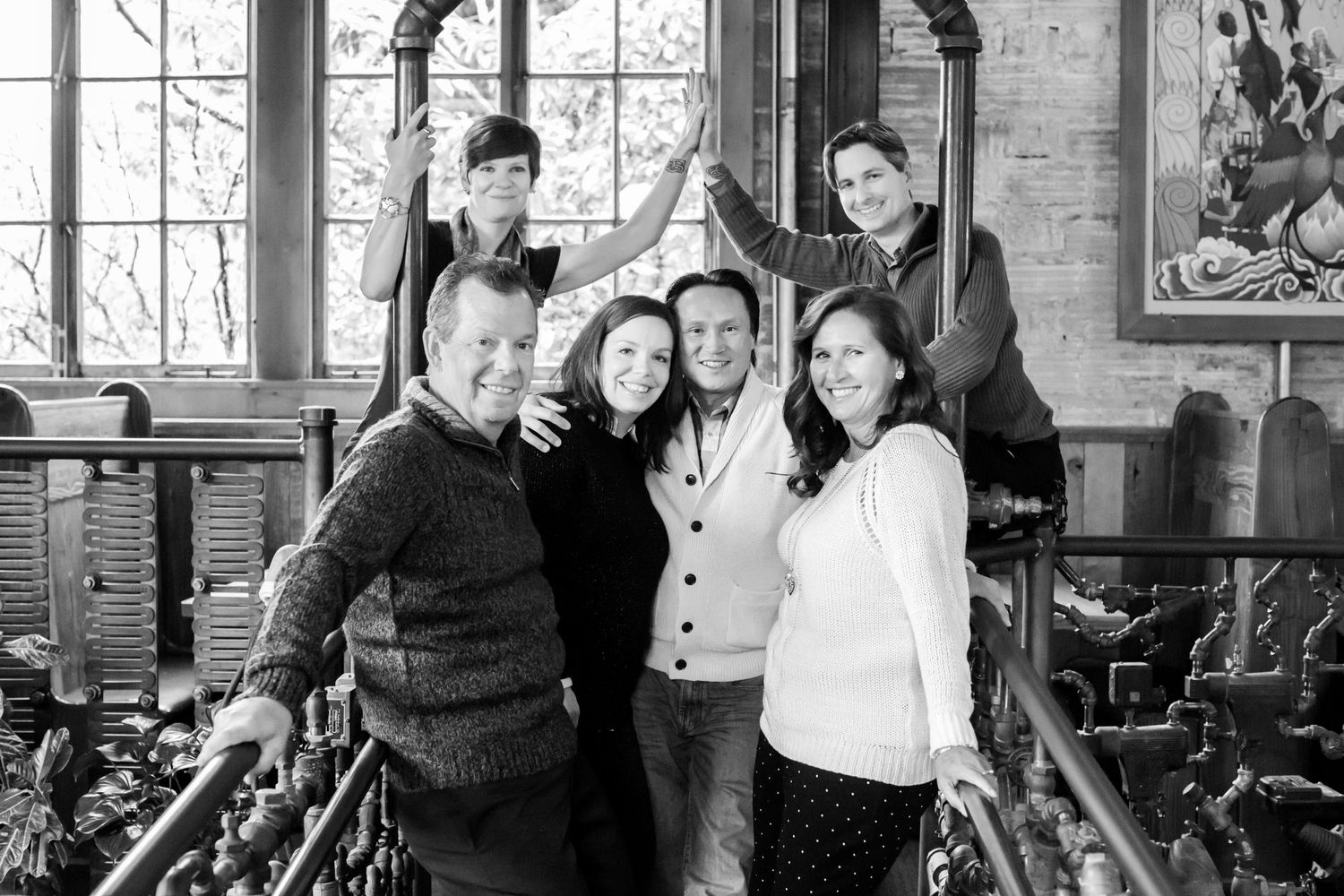 Black and white photo of a casual group gathering indoors near a decorative window.