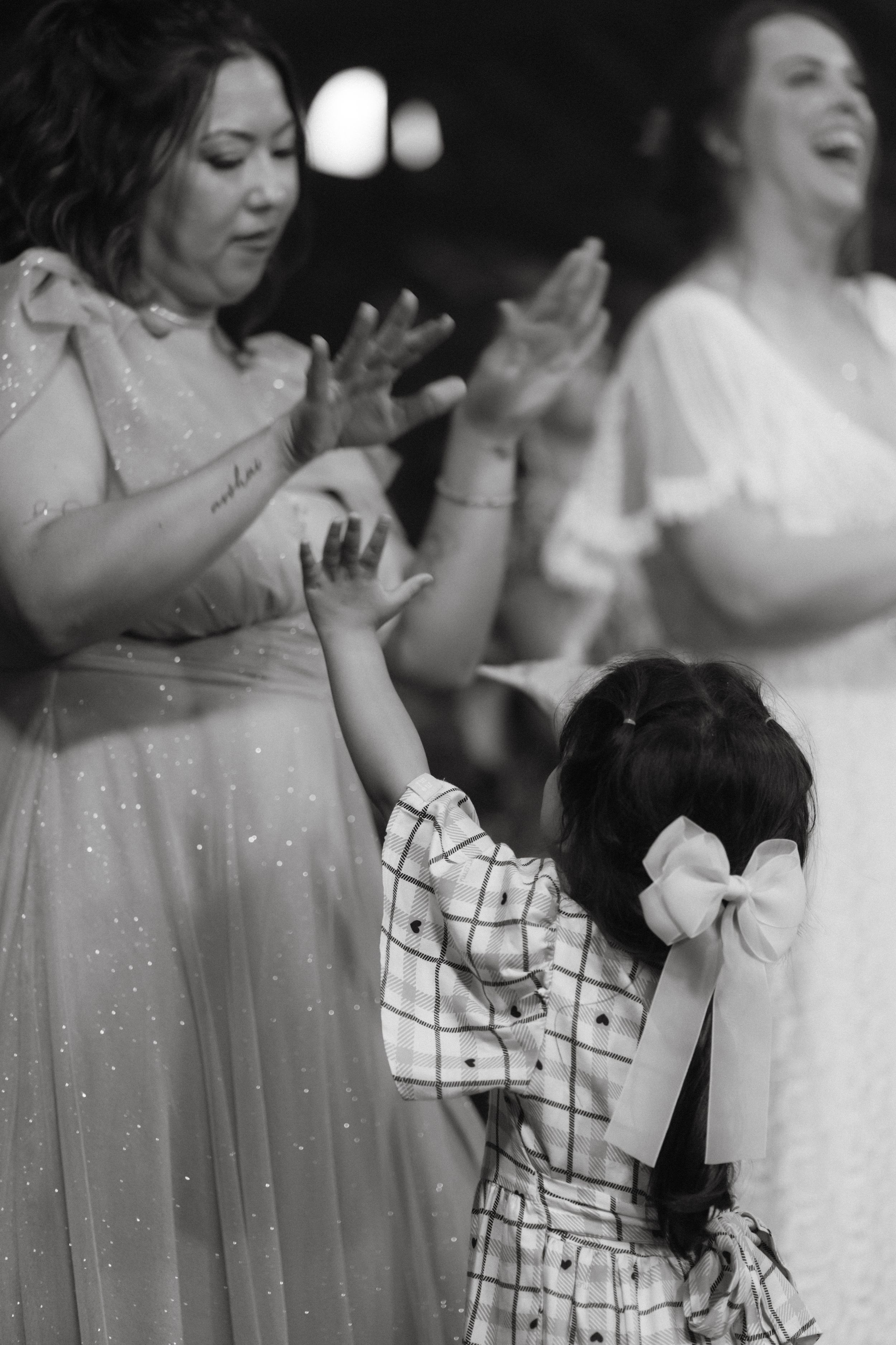 Black and white photo of wedding guests dancing with a small child in a checked dress.