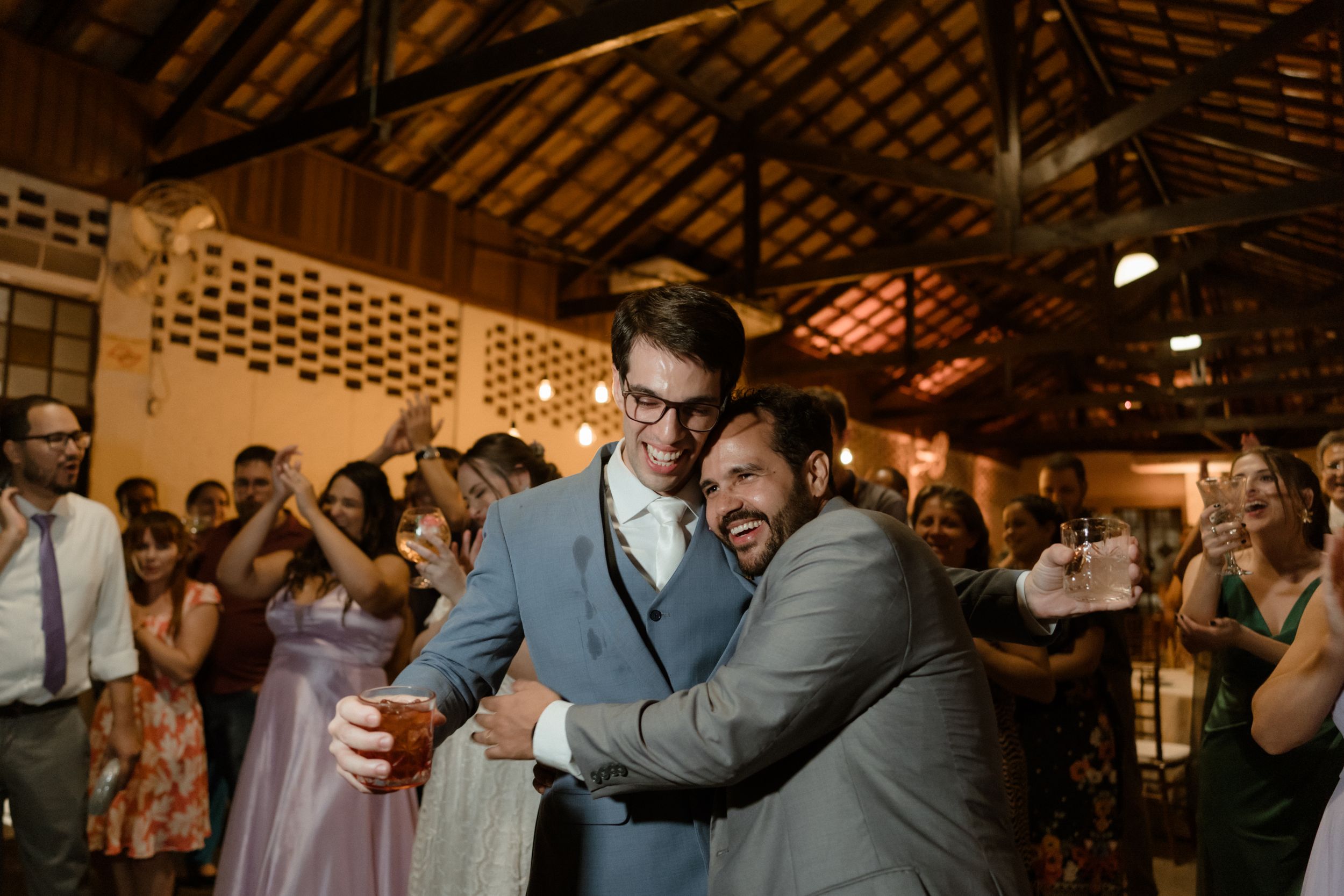 Wedding guests celebrate with drinks at a rustic indoor reception venue.