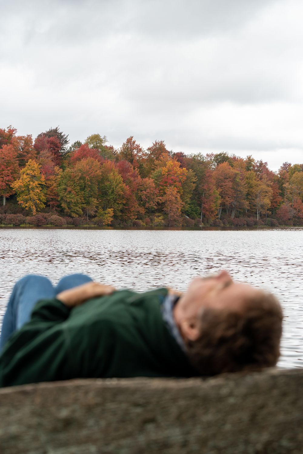 Person resting on rock overlooking lake with colorful fall foliage in background.