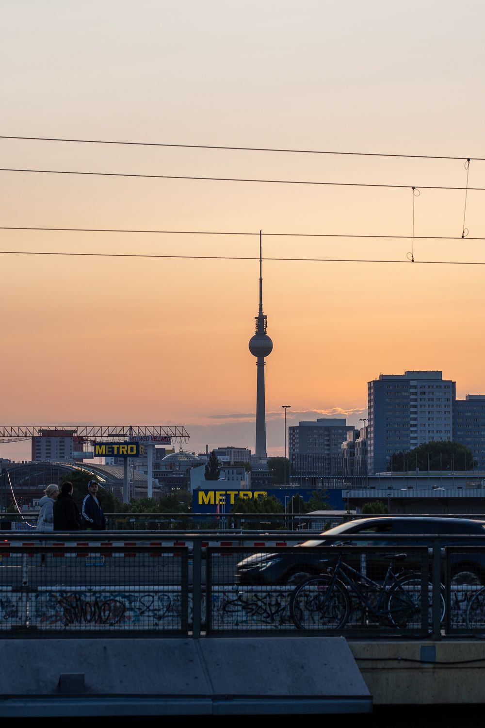 Berlin TV Tower silhouetted against orange sunset sky with urban skyline.