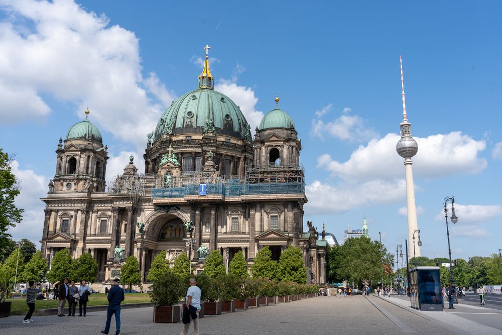 Berlin Cathedral and TV Tower stand against blue sky with white clouds in iconic cityscape view.