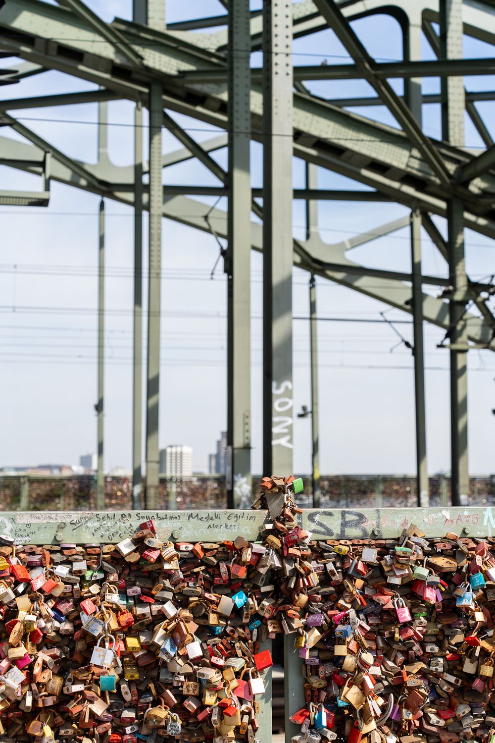Love locks attached to bridge railing with industrial metal structure in background.