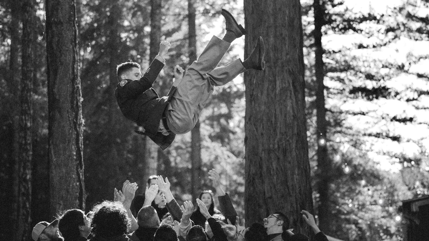Black and white photo of performer jumping above crowd in forest setting.