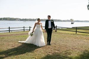 Couple walks along a scenic waterfront path during their wedding photoshoot at sunset.