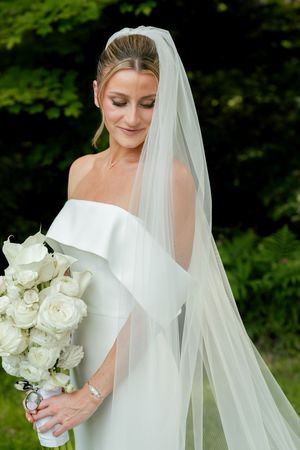 Bride in elegant white dress holds classic white rose bouquet.