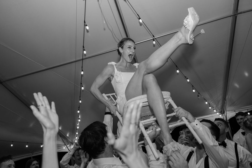 Wedding reception celebration with guests dancing and raising hands under string lights.