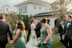 Wedding party gathers outside a Spanish-style villa with terra cotta roof during golden hour.