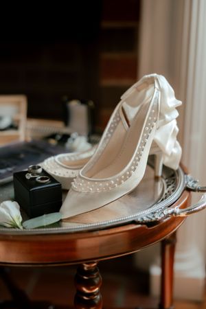 White pearl-embellished bridal heels displayed on vintage wooden table with decorative elements.