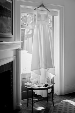 Classic white wedding dress hanging in doorway with natural light streaming through window.