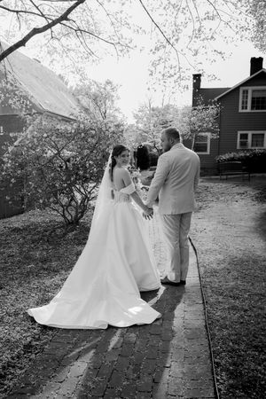 Bride and groom walking hand in hand on outdoor pathway in black and white.