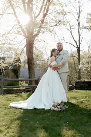 Wedding couple embracing on sunny lawn with trees and natural lighting.