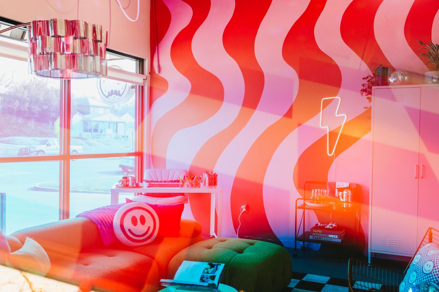 a funky, vibrant lounge with a wavy pink and red wall mural, a neon lightning bolt light, and natural light from the nearby windows