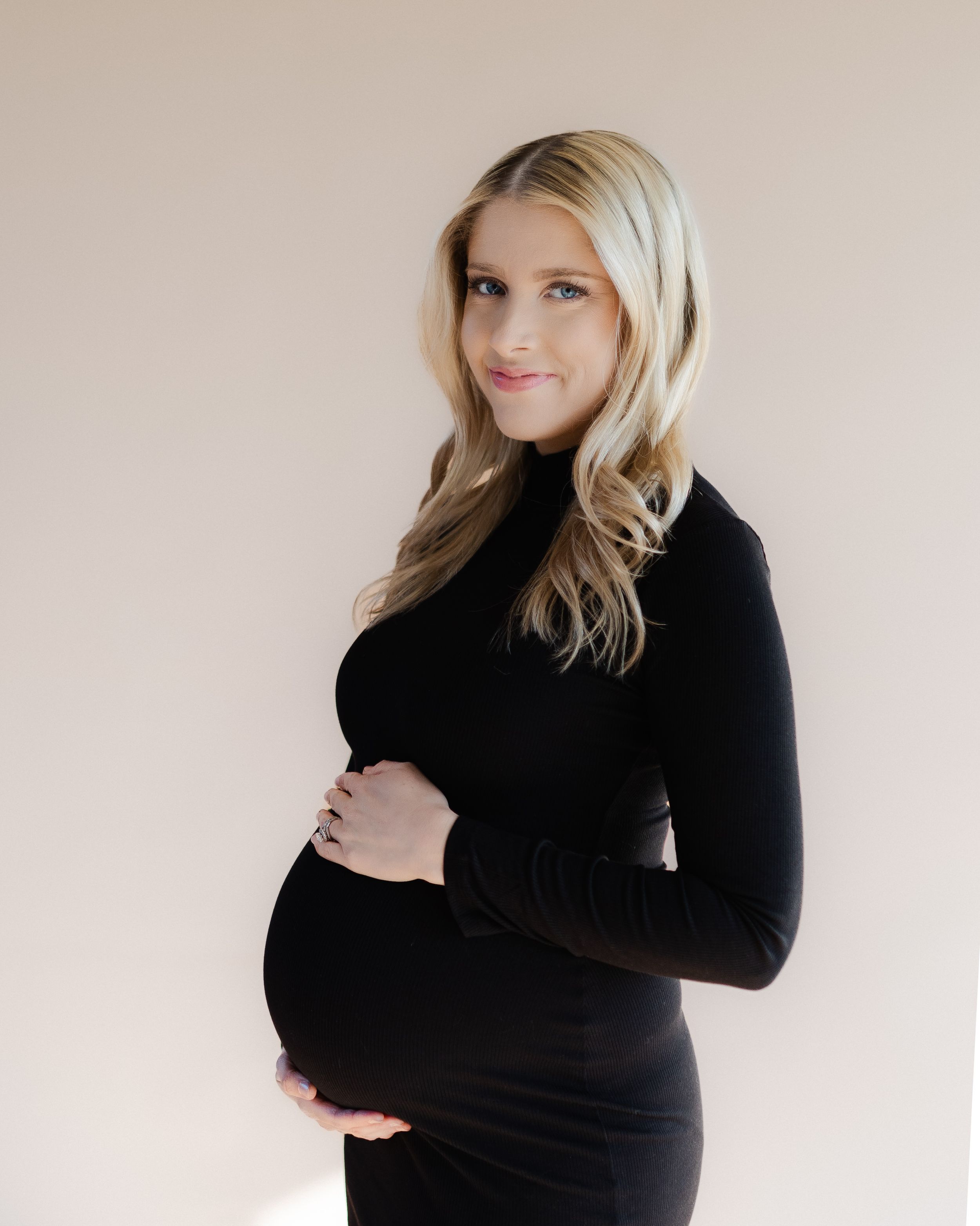 Maternity portrait in black turtleneck against neutral background.