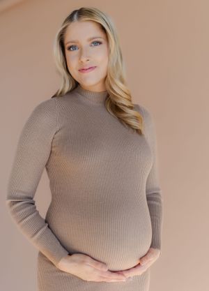 Maternity portrait in a beige ribbed sweater against neutral backdrop.