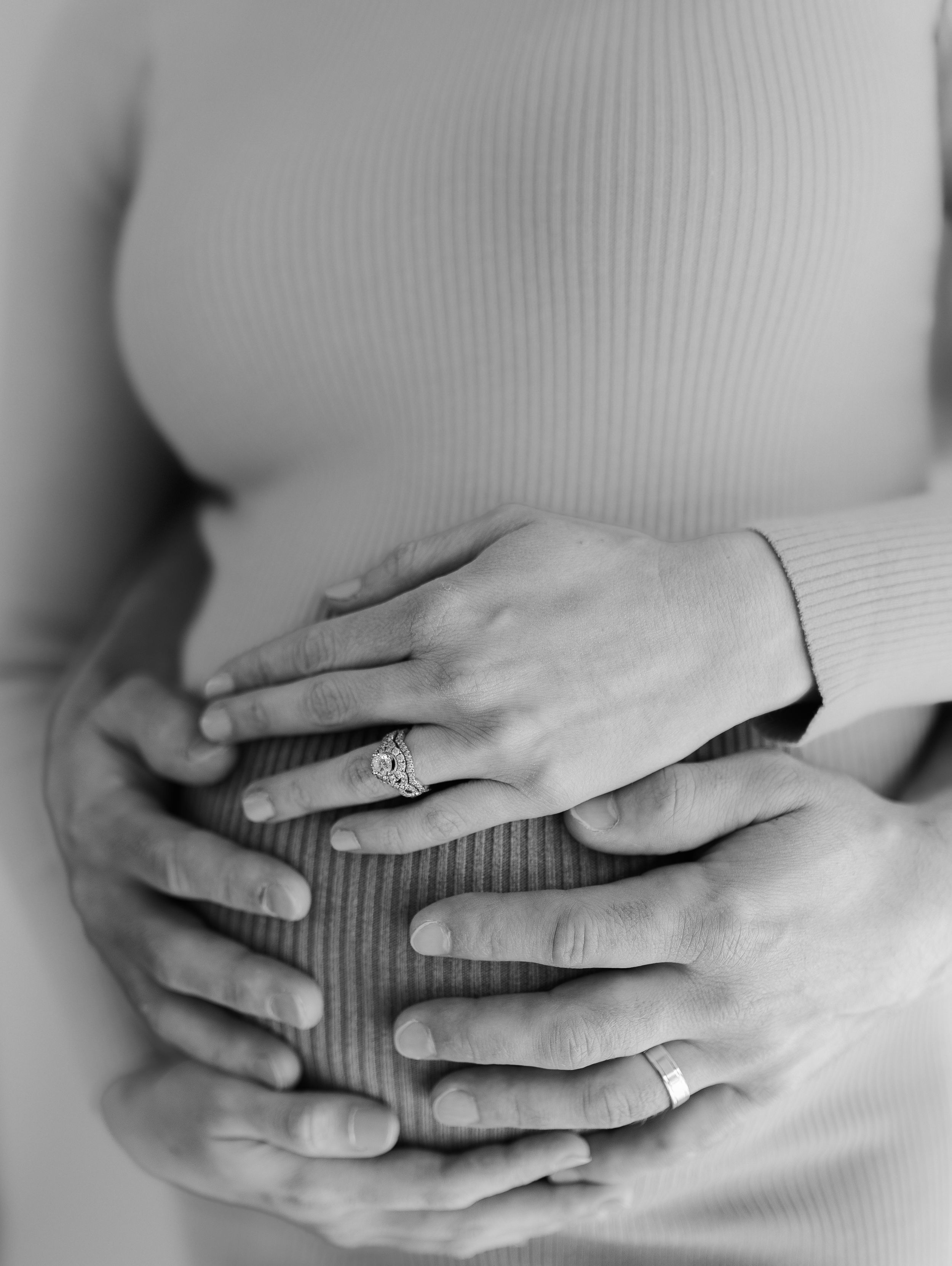 Close-up of hands with engagement ring resting on a ribbed sweater.