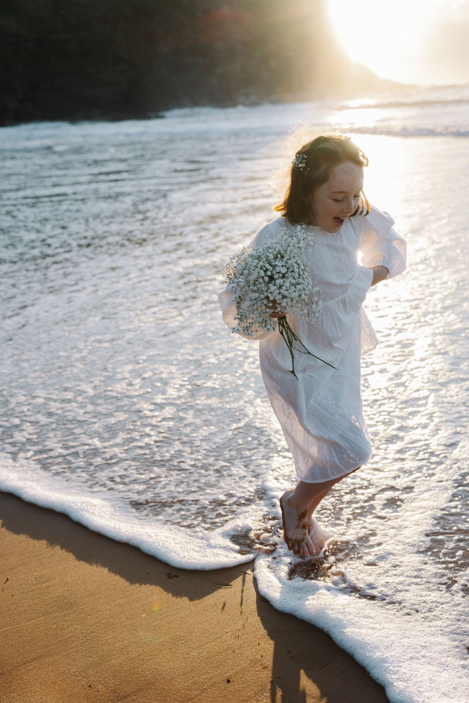 Family Photography - Playful Girl holding flowers running through the water at Bilgola Beach, Northern Beaches, Sydney