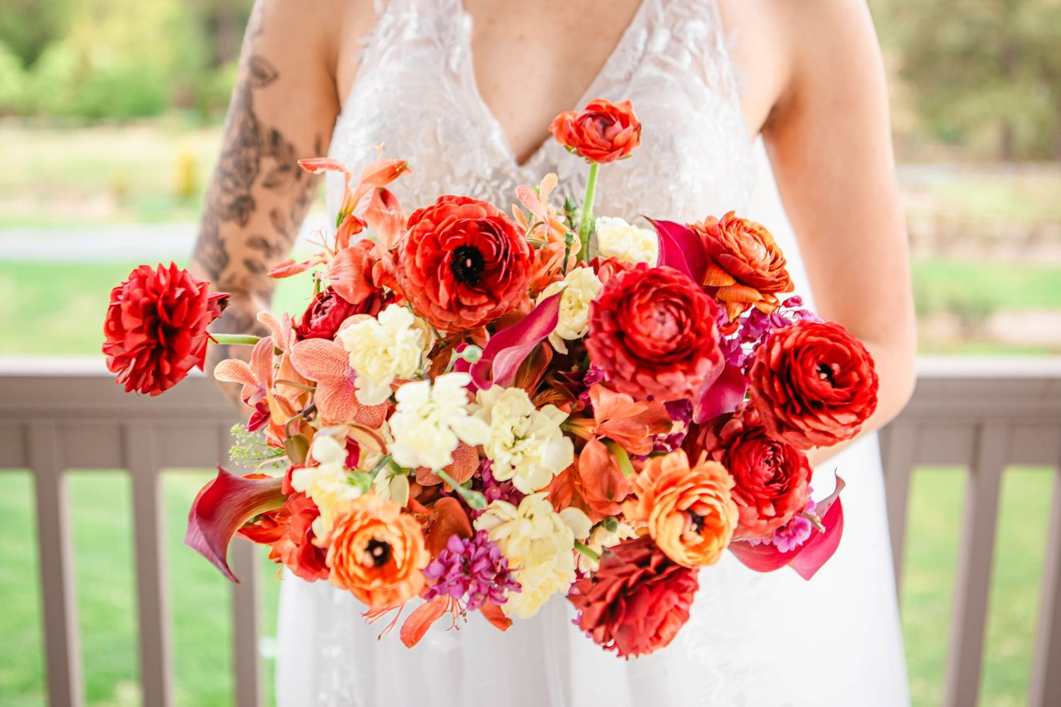 Colorful wedding bouquet featuring red, orange and cream roses in a rustic outdoor setting.
