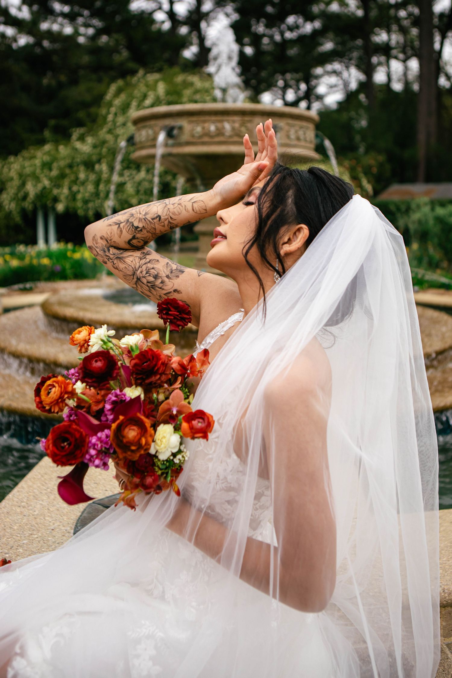 Artistic bridal portraits with vibrant red and orange bouquet against garden backdrop.