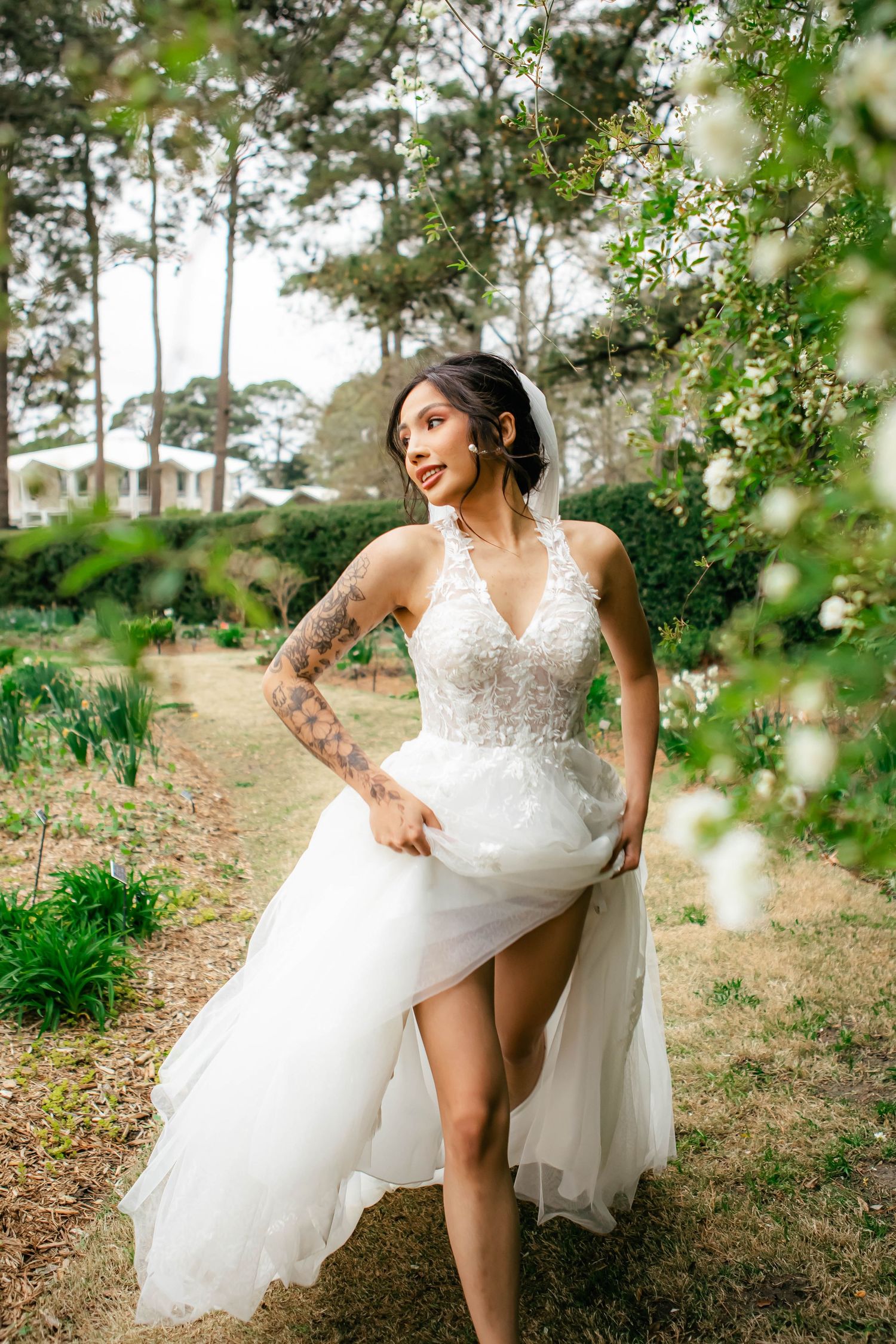 Bride in white lace gown shows leg through slit on garden path.