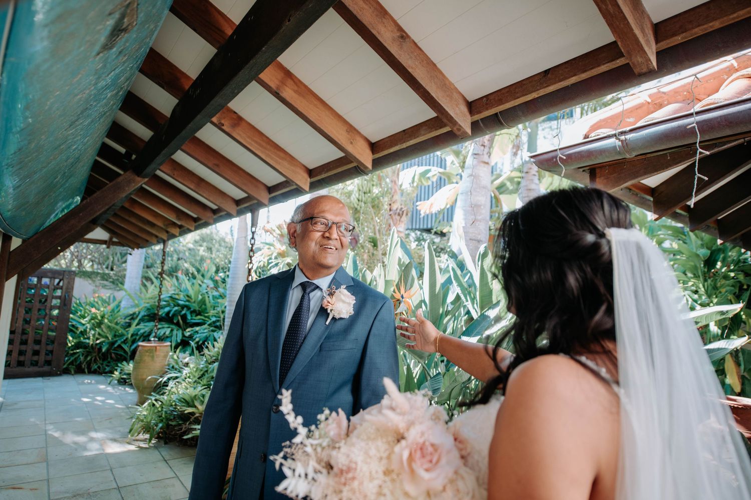 Wedding couple sharing a romantic moment under a covered patio with tropical greenery.