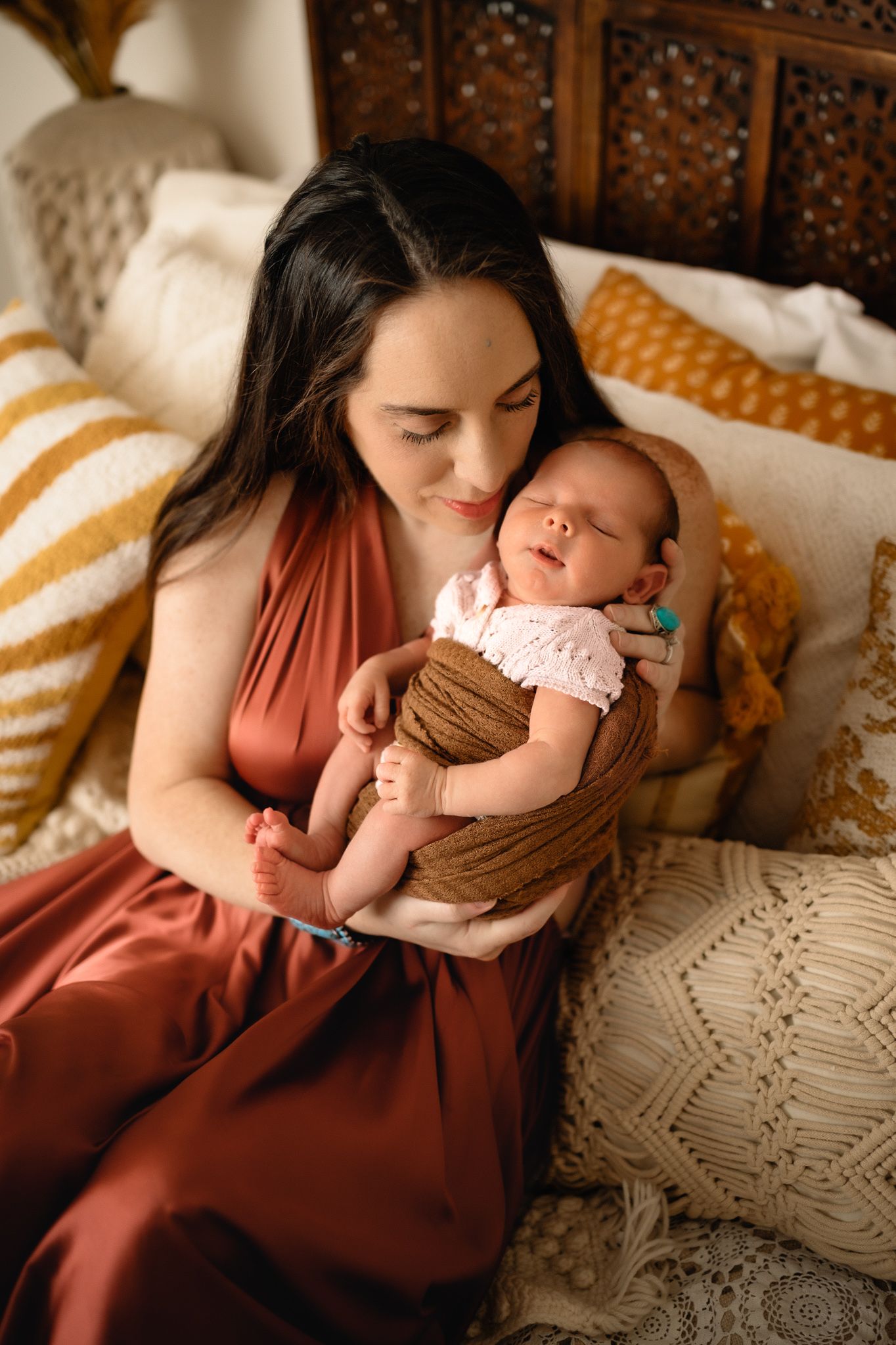 Tender moment with sleeping newborn wrapped in brown fabric on textured bedding.