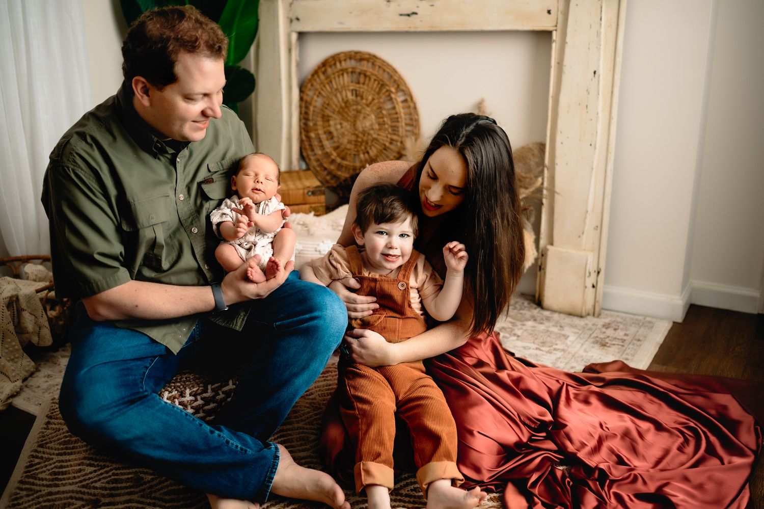 A cozy indoor family photo shoot with parents and children sitting on a burgundy blanket.
