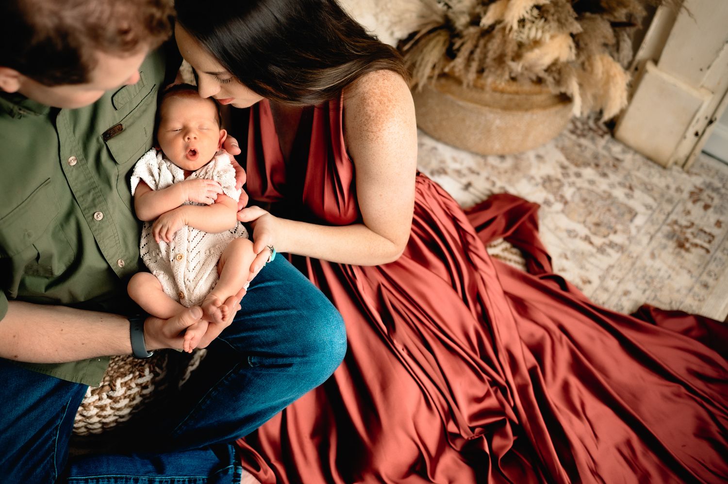 Intimate portrait of parents cradling a newborn baby on a red blanket.