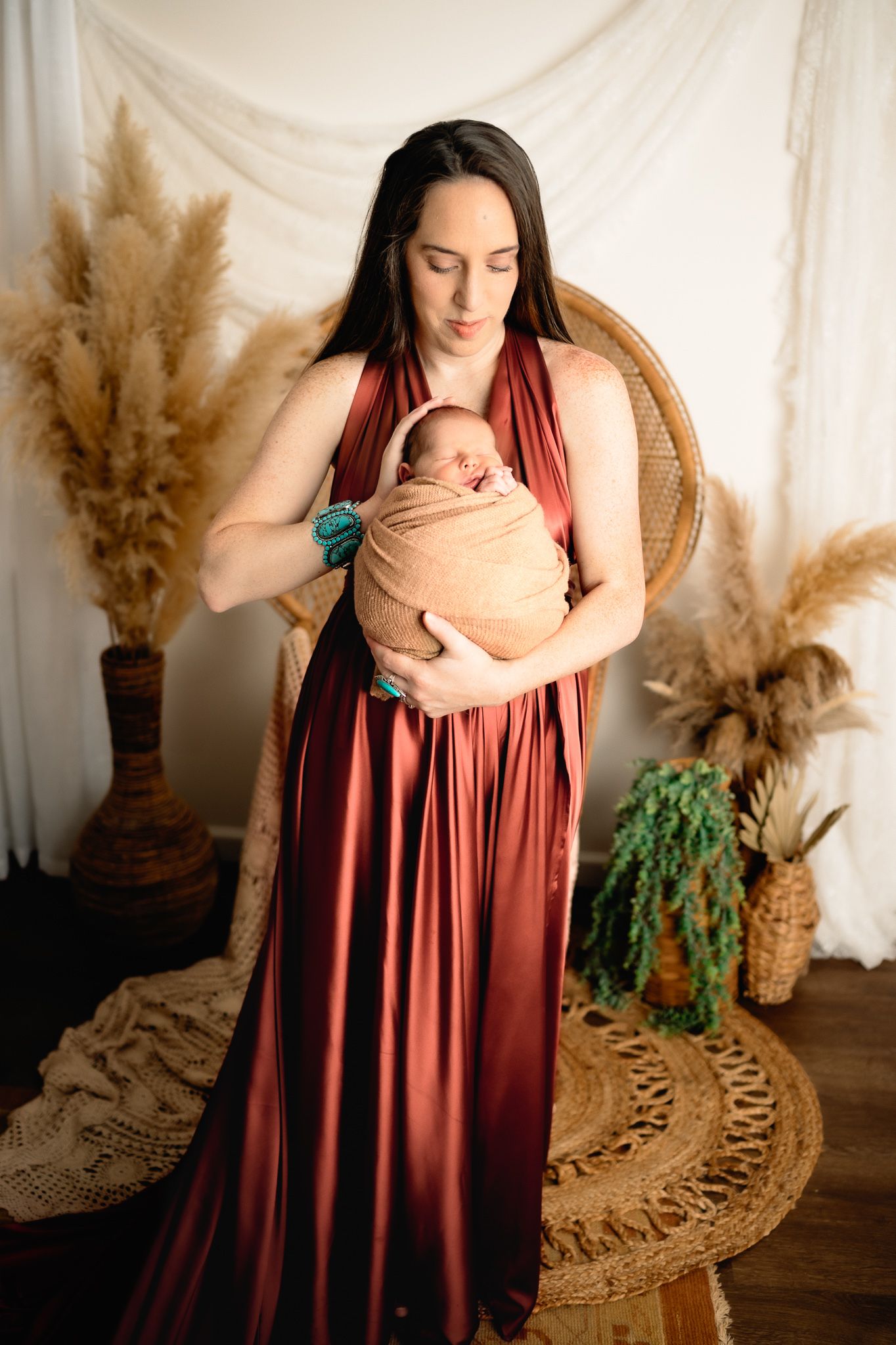 A tender moment with mother in burgundy dress holding swaddled newborn.