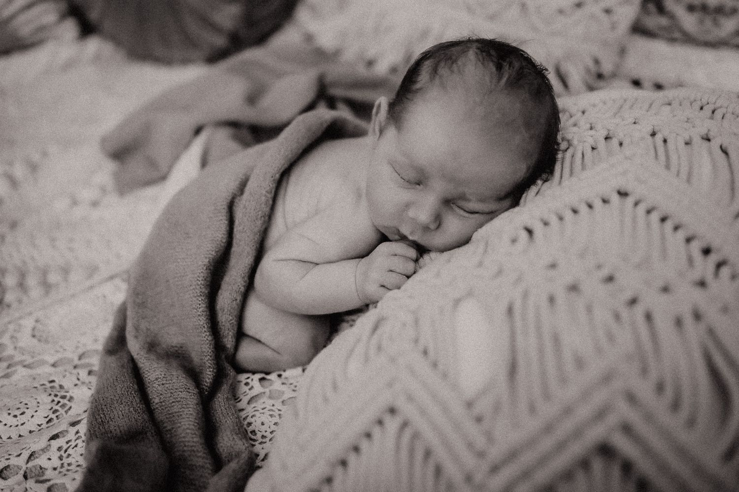 Black and white portrait of sleeping newborn on textured blanket.