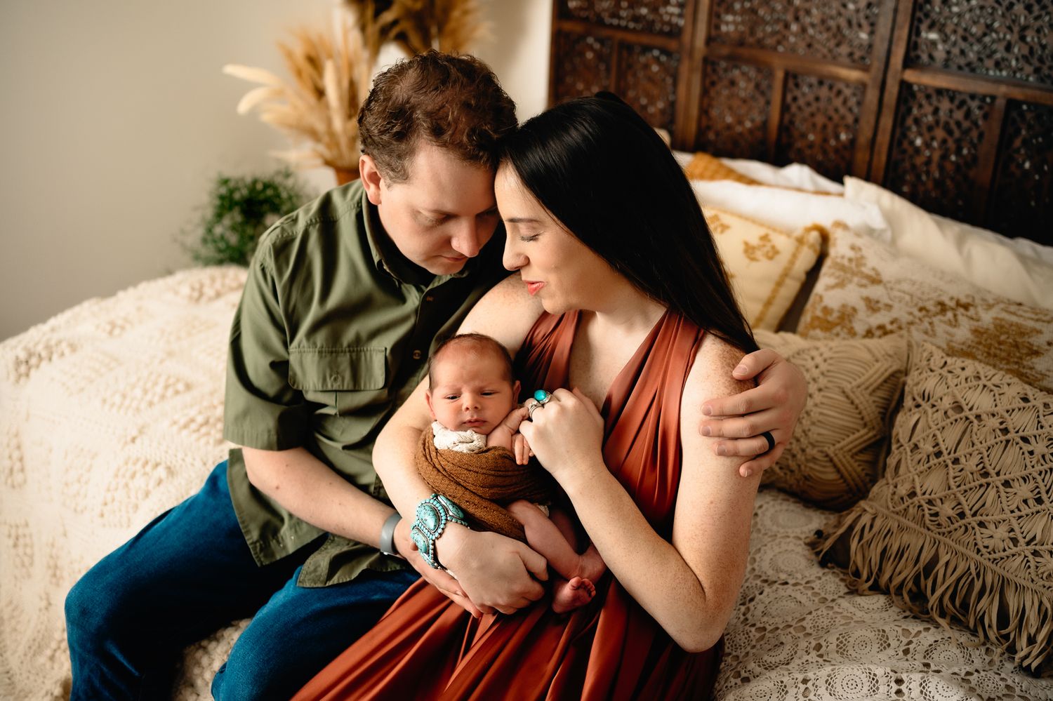 Intimate indoor family moment with newborn baby on textured bedding and wooden decor.