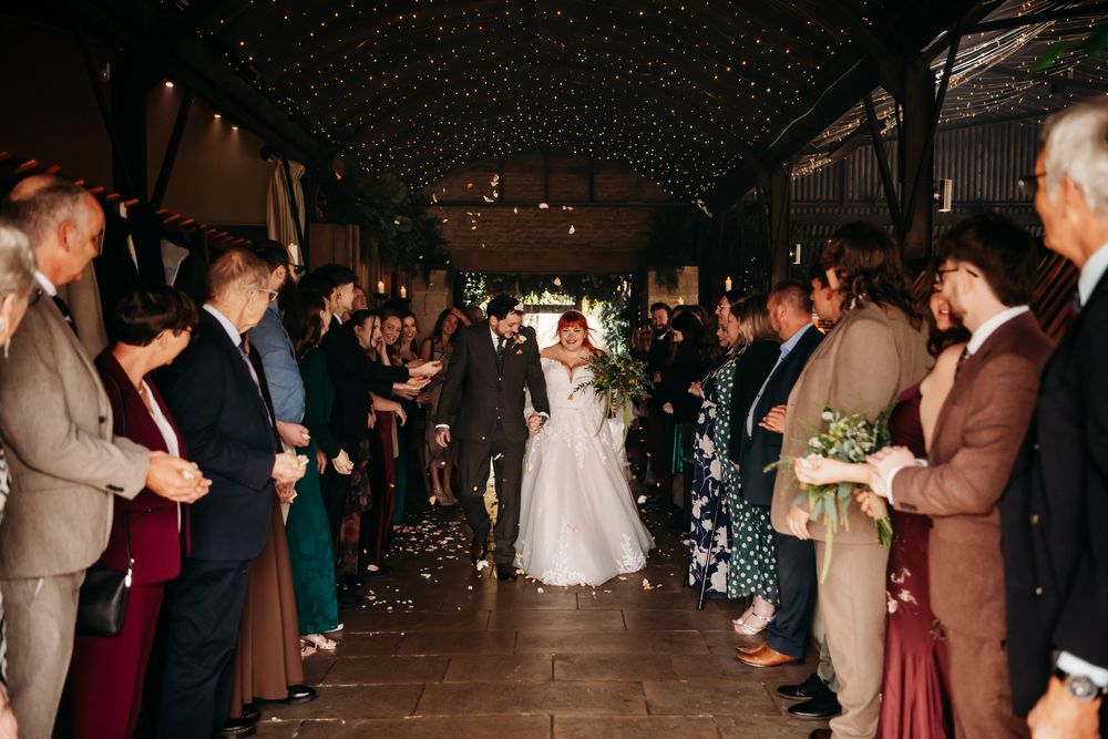 Wedding guests line up along a dark aisle creating a tunnel effect during an indoor reception celebration.