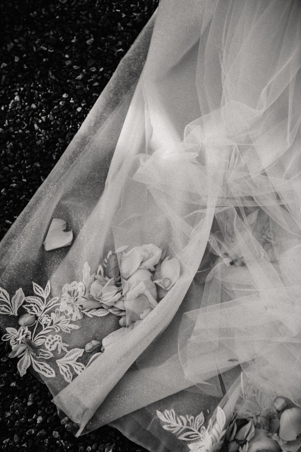 Black and white detail shot of delicate wedding dress veil with floral embroidery and tulle fabric against dark background.