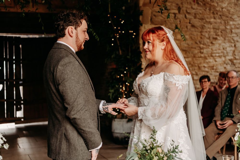 A couple shares an intimate moment during their wedding ceremony in a rustic brick-walled venue with twinkling lights.