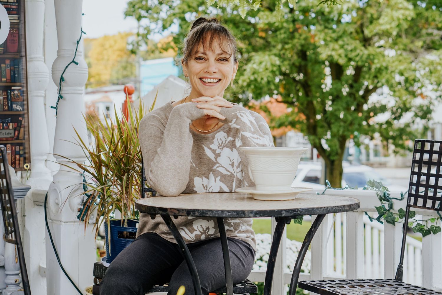 Person enjoying coffee and pastry at outdoor cafe table with greenery in background.