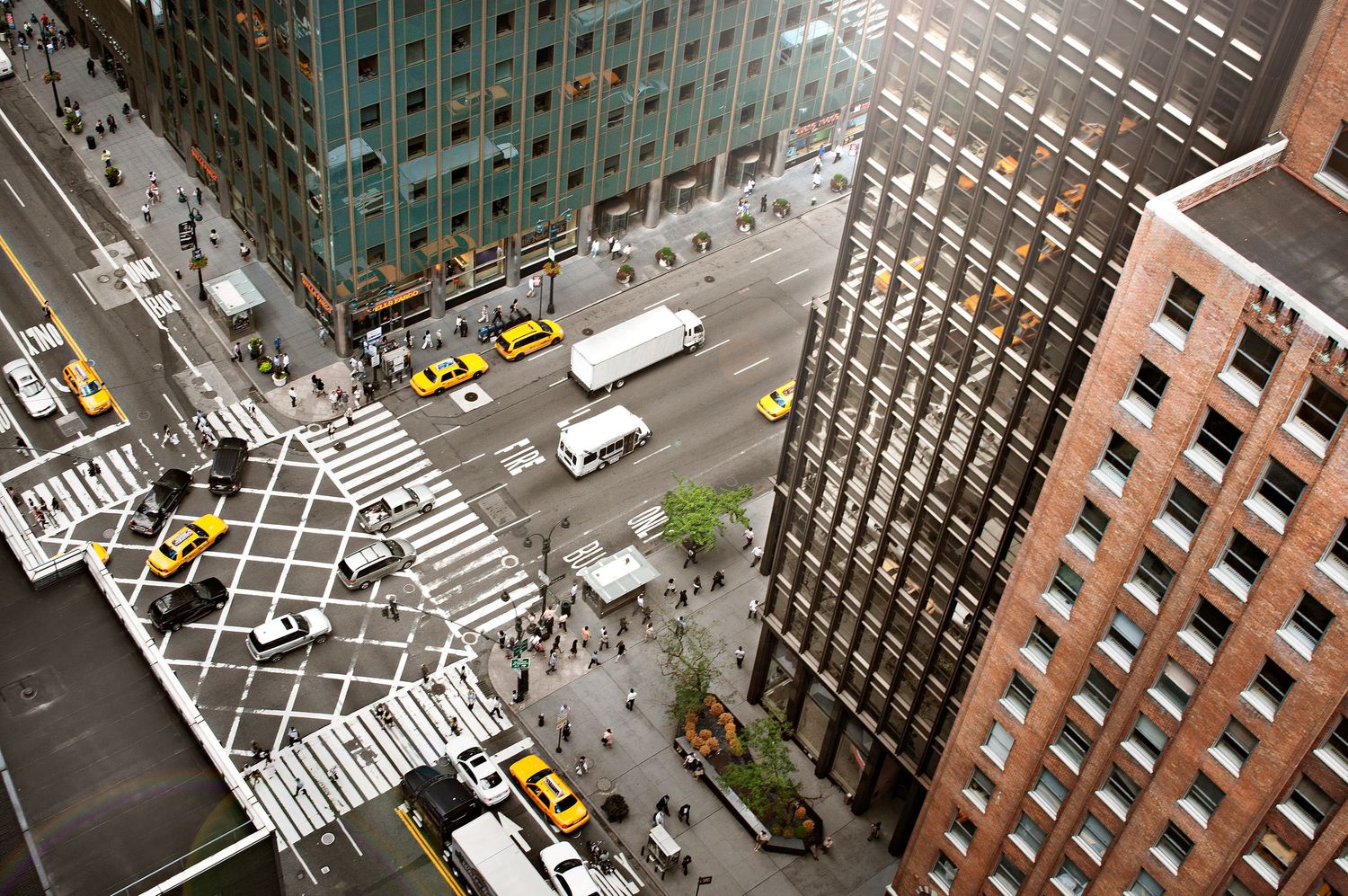 Aerial view of city intersection with yellow taxis and pedestrian crossings from above.