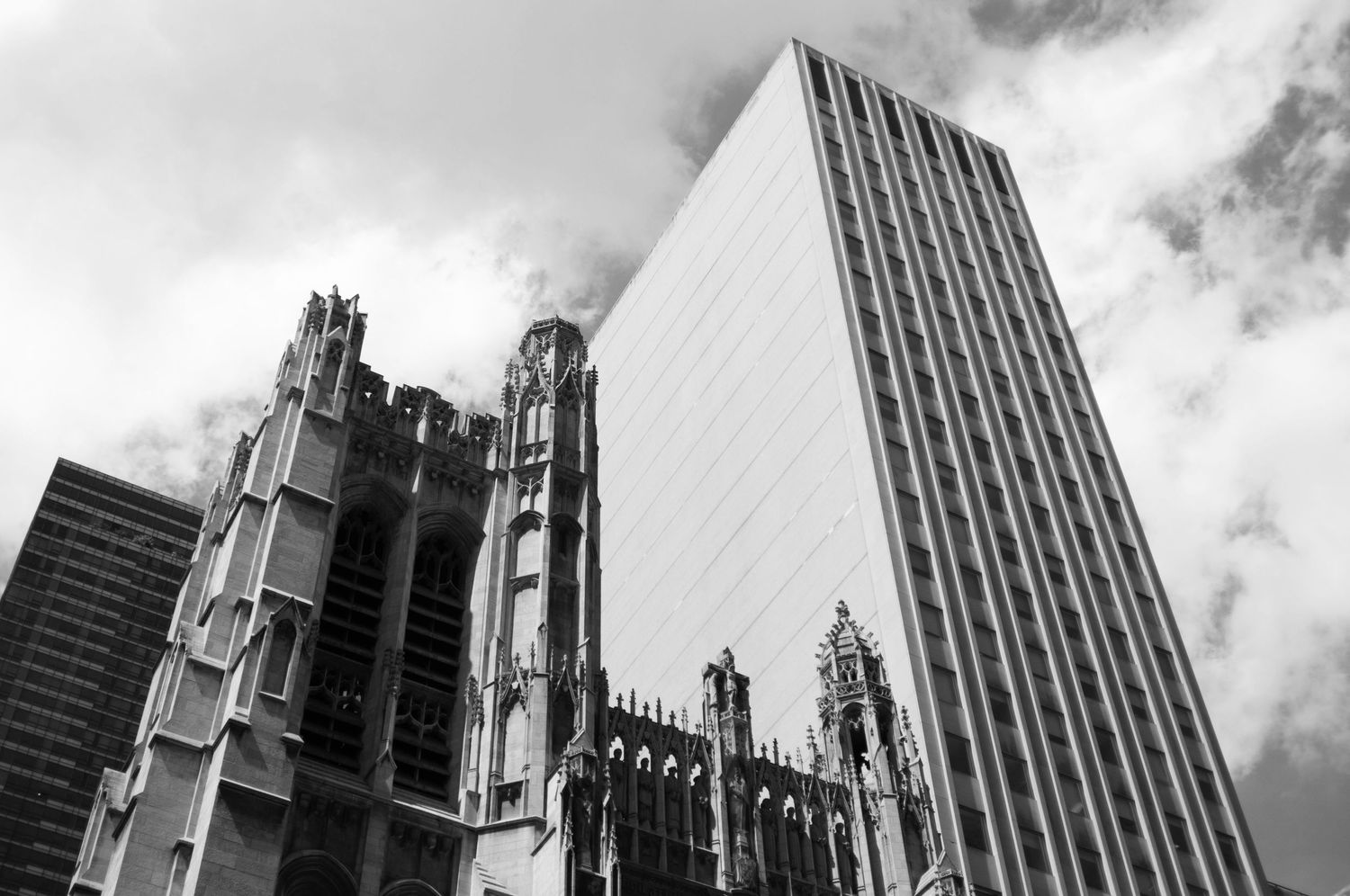Dramatic upward view of skyscrapers and office buildings in black and white against cloudy sky.