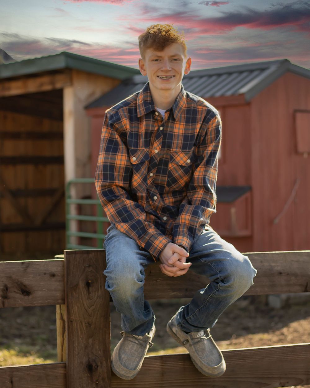 A teenage boy sits on the top rail of a fence