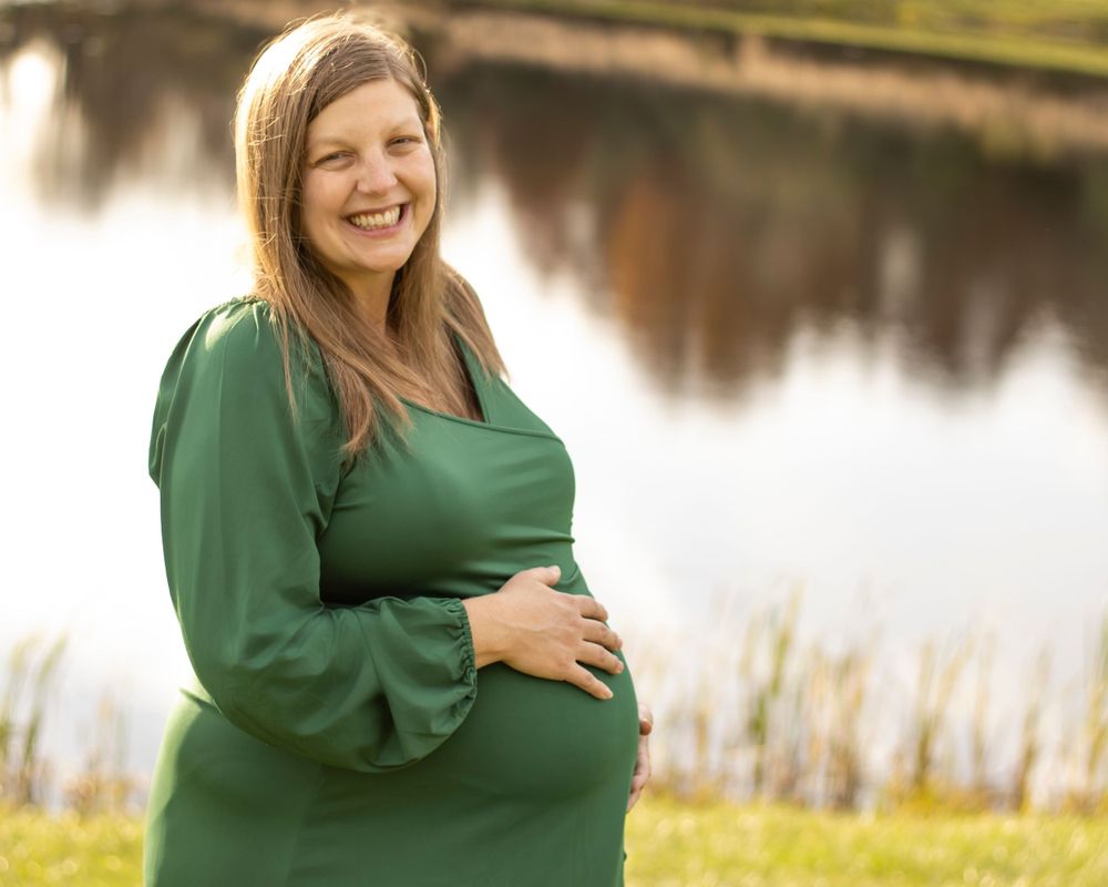 An expectant mother rests her hand on her stomach in front of a pond