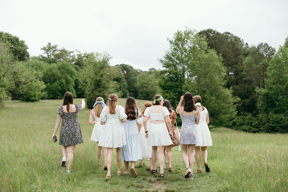 A group walks together across a sunny meadow wearing light colored clothing. Le Château du Cœur Wedding Photographer