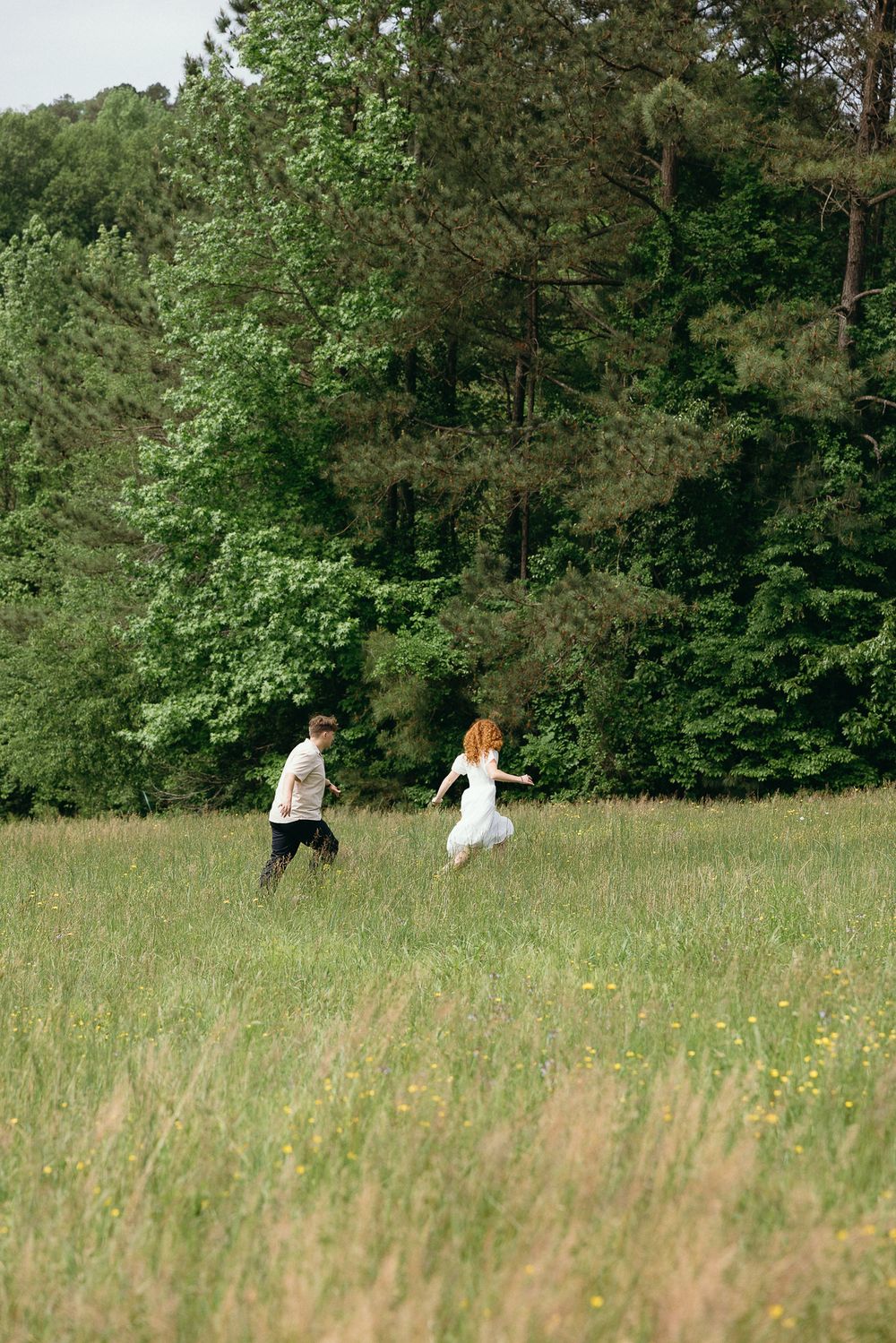 A distant view of two people walking through a green meadow bordered by forest. Le Château du Cœur Wedding Photographer
